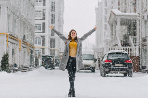 Happy snowing winter time in big city of pretty girl enjoying snowfall on street. True positive emotions, holding hands above, smiling with closed eyes, love your life, waiting for christmas, winter holidays.